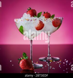 Zwei hohe Cocktailgläser mit einem Cocktail, verziert mit frischen Erdbeeren und Pfefferminzblättern auf einem klaren, reflektierenden schwarzen Hintergrund. Stockfoto