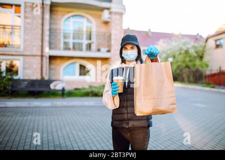 Gesundheitsschutz, Sicherheit und Pandemie Konzept - Lieferung Frau in schützende Gesichtsmaske und Handschuhe mit einer Tasche von Lebensmitteln und Kaffee Stockfoto