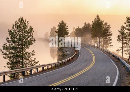 Finnische Landschaft mit schmaler Autostraße durch den See. Stockfoto