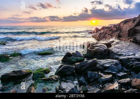 Küste des Ozeans bei Sonnenuntergang. Schöne Landschaft mit Felsen im Wasser. Herrliche Wolkenlandschaft über Sonne und Horizont. Konzept der Ruhe und medi Stockfoto