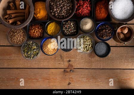 Schalen mit Salz, schwarzem Sesam, Mohn, Kürbiskernen, roten trockenen Chilis, Goji-Beeren, Curry, Koriander, Bahari, Kardamom, Knoblauch und Kurkuma auf Stockfoto