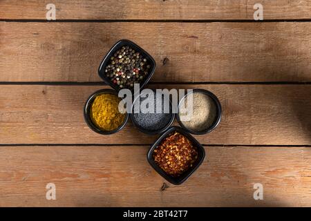 Fünf kleine Schalen mit Mischung aus Paprika, weißem Pfeffer, roten trockenen Chilis, Welpensamen und Curry auf einer Holzfläche Stockfoto