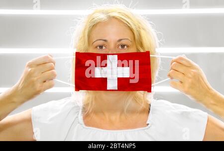 Frau auf Weiß mit Schweizer Flagge auf einer Operationsmaske. Konzept des Ausbruchs und der Quarantäne für die Coronavirus-Pandemie in der Schweiz. Antiviral Stockfoto