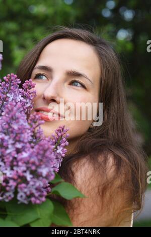 Das Gesicht eines glücklichen lächelnden jungen schönen Mädchen mit Ein Busch blühender Flieder Stockfoto