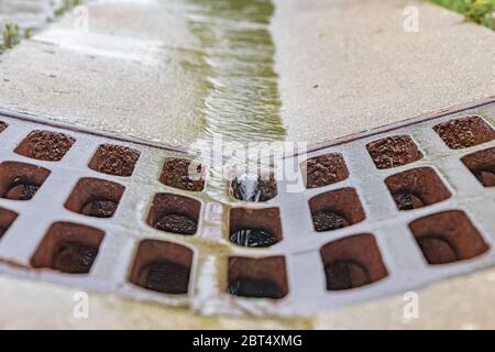 Nahaufnahme von Regenwasser, das in die Rinne der Straße fließt und in das Regenwasserkanalrost fließt. Stockfoto