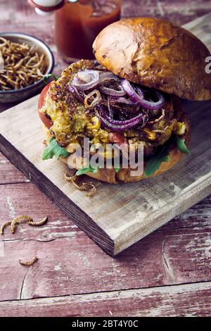 Trendy Bug oder Insekt Burger mit knusprig gebratener Mehlwürmer und Salat Schneiden auf ein frisches knuspriges Brötchen auf einem urigen und Tisch mit Kopie Raum fo serviert. Stockfoto