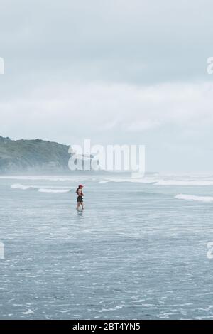 Frau steht in der Meeresbrandung, Mangawhai Heads, Northland, North Island, Neuseeland Stockfoto