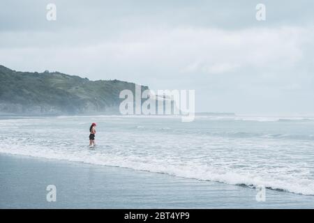 Frau steht in der Meeresbrandung, Mangawhai Heads, Northland, North Island, Neuseeland Stockfoto