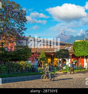 Stadtleben in Antigua mit einem älteren Mann, der während einer Vulkanascheexplosion und eines Ausbruchs des Fuego Vulkans in Guatemala Fahrrad fährt. Stockfoto