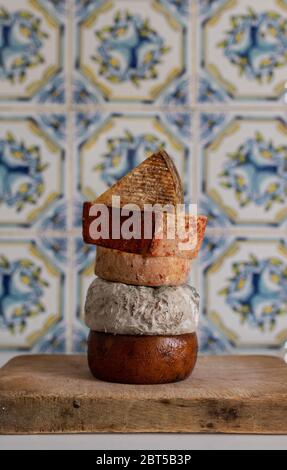 Verschiedene Käsesorten. Verschiedene Käseturm auf einem Holzbrett vor einer rustikalen Fliesenwand. Stockfoto