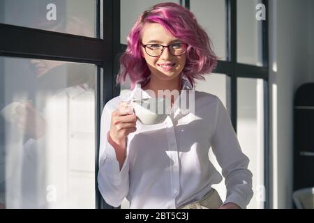 Lächelndes junges Hipster jugendliches Mädchen, das weißes Hemd und Brille trägt, stehen im Büro. Stockfoto