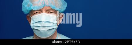 Erfahrene Senior Erwachsene Arzt gekleidet medizinischen Gesicht chirurgische Maske und Kappe. Vorbeugender Schutz vor ansteckender Krankheit, Coronavirus. Panorama Stockfoto