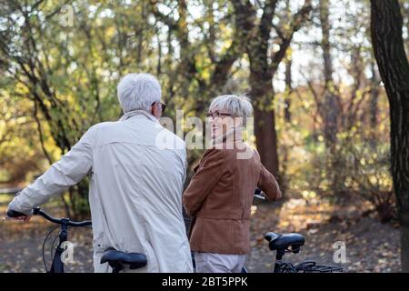 Altes Paar mit Fahrrädern, die im Park spazieren gehen Stockfoto