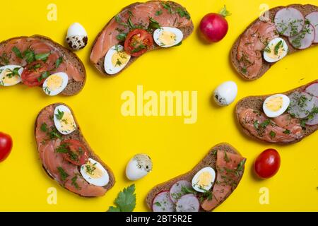 Sechs Brote mit Lachs, Wachteleier und Gemüse. Auf gelbem Papier, Draufsicht. Gelbes Papier Stockfoto