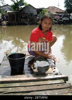 Junges Mädchen, das Wäsche mit verschmutztem Wasser in Slum neben dem Kalimas-Fluss surabaya java indonesia macht Stockfoto