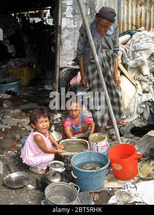 Alte Dame mit kleinen Kindern in dreckigem, mit Müll gefüllten Hütte im Slum neben dem Kalimas Fluss surabaya java indonesia Stockfoto