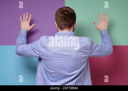 Der Mann in einem blauen Hemd steht mit dem Rücken zur Kamera und hebt die Hände hoch, macht eine Geste der Hingabe. Stockfoto