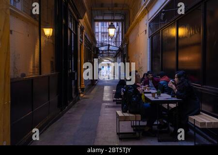 Paris, Frankreich - 2. Nov 2019: Ein traditioneller Pariser Durchgang mit wenigen Leuten, die einen Kaffee trinken. Foto am frühen Abend mit Licht an und große da Stockfoto