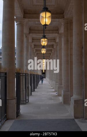 Paris, Frankreich - 2. Nov 2019: Eine traditionelle Pariser Arkade mit Lichtern an und einem Mann aus der Ferne. Foto aufgenommen im Palais-Royal, am frühen Abend Stockfoto