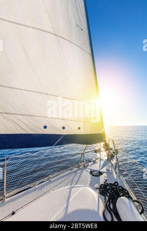 Segeln mit der Sonne. Blick vom Deck der Yacht auf den Bug und die Segel. Segelboot mit aufgesetzten Segeln, die im offenen Meer gleiten. Griechenland, Europa Stockfoto