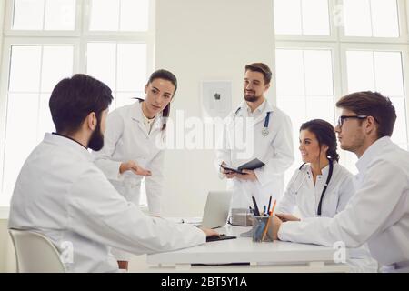 Gruppe von Praktizierenden Ärzten in einem Treffen diskutieren die Diagnose eines Patienten am Schreibtisch in einem Klinikbüro sitzen. Selbstbewusste Ärzte auf der Konferenz ta Stockfoto