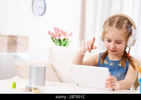 Schönes Kind, das mit dem Finger auf das Tablet zeigt und mit Kopfhörern Spiele spielt Stockfoto