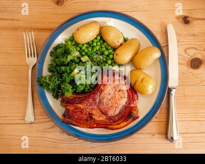 Mittagessen Hauptgericht Schweinefleisch Chop mit Lockenkohl, Gartenerbsen neue Kartoffeln, und Soße Stockfoto