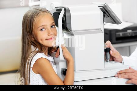 Kleines blondes Mädchen mit einem speziellen modernen Diagnosegelgerät in der Augenklinik Stockfoto