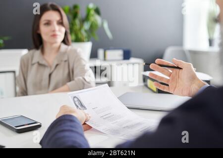 Hände der zeitgenössischen Psychologin oder Arbeitgeber mit Stift und Lebenslauf der jungen weiblichen Bewerber erklären etwas während des Interviews Stockfoto