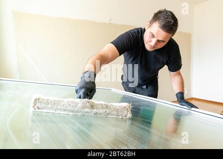 Ein professioneller Fensterreiniger, der eine Scheibe Reinigung Waschmaschinenhülle verwendet, um ein großes zusammenklappbares Wohnungsfenster zu reinigen Stockfoto