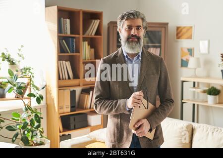 Serious reifen männlichen Profi in formalwear halten Brillen und Zwischenablage mit Dokument, während vor der Kamera stehen Stockfoto