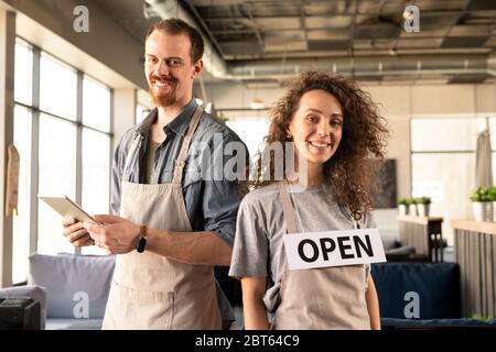 Zwei erfolgreiche junge Besitzer von luxuriösen Restaurant in Arbeitskleidung stehen vor der Kamera auf Hintergrund der Sofas und Interieur Stockfoto