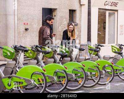 Ein Paar, das sich auf den Verleih von elektrischen Stadtfahrrädern "Vélib" in der Rue Jacques Callot, Paris 6, Frankreich vorbereitet. Stockfoto