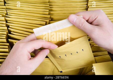 Qualitätsprüfung des selbstverschlossenen Versandumschlags. Männliche Hände öffnen eine gelbe Blase Mailer aus einem Haufen von Versand Luftpost-Pakete. Nahaufnahme, t Stockfoto
