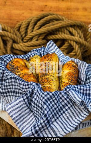 In Teig gebackene Würstchen, mit Salz und Mohn bestreut, in rustikaler Zusammensetzung. Würstchenbrötchen, leckeres hausgemachtes Gebäck. Stockfoto