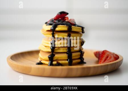 Stapel von flauschigen Frühstück amerikanische Pfannkuchen mit Erdbeeren und Schokoladensauce Sirup Gießen von oben auf einem Holzteller mit Erdbeeren in Scheiben geschnitten Stockfoto