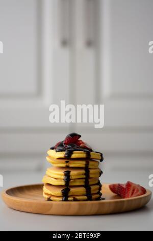 Stapel von flauschigen Frühstück amerikanische Pfannkuchen mit Erdbeeren und Schokoladensauce Sirup Gießen von oben auf einem Holzteller mit Erdbeeren in Scheiben geschnitten Stockfoto