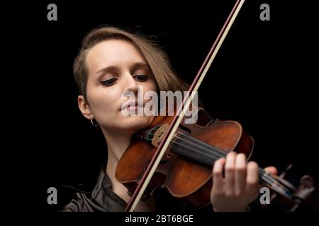 Professionelle leidenschaftliche Geigerin, die auf einer Barockgeige während einer klassischen Aufführung oder Probe vor schwarzem Hintergrund mit Fokus spielt Stockfoto