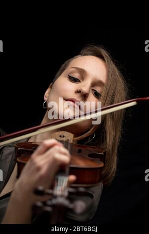 Engagierte leidenschaftliche professionelle Geigerin spielt eine antike handgefertigte Holzbarocke Geige während einer Live-Performance in Nahaufnahme auf Schwarz Stockfoto