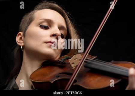 Engagierte Bratschistin, die während einer Live-Aufführung eine Barockvioline spielt, die ihre Leidenschaft für das Instrument hautnah und mit Fokus auf ihr Gesicht genießt Stockfoto