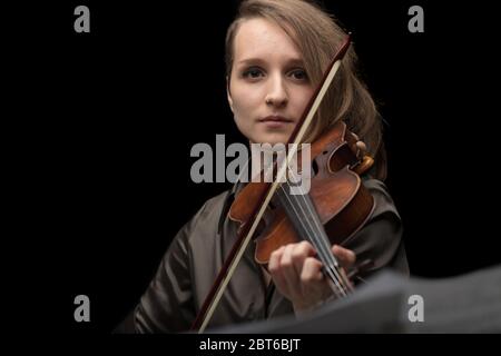 Attraktive professionelle Geigerin auf einer Barockvioline während eines klassischen Musikrezital auf schwarzem Hintergrund Stockfoto