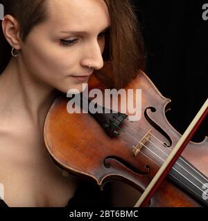 Frau mit durchbohrter Nase, die während einer Live-Aufführung oder einem Recital eine klassische Geige spielt, in der Nähe ihres Gesichts und Instruments Stockfoto