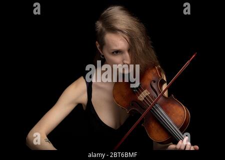 Leidenschaftliche professionelle Musikerin, die während einer Live-Aufführung eine Barockvioline in einem Nahaufnahme-Blickwinkel auf schwarzem Hintergrund spielt Stockfoto