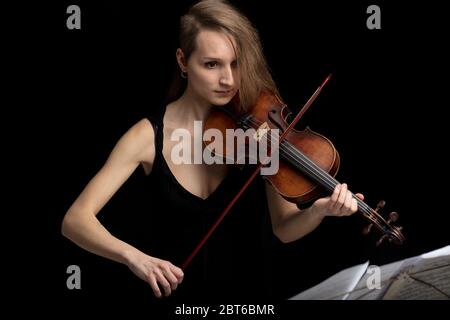 Engagierte Frau, die eine antike Barockgeige während einer klassischen Musikaufführung in einem hohen Winkel ihrer Lesung aus der Partitur gegen eine BL spielt Stockfoto