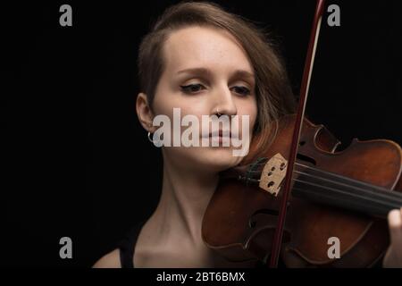 Porträt einer engagierten professionellen Geigerin, die auf einer klassischen antiken Barockgeige vor schwarzem Hintergrund in einem Live-Recital oder Con spielt Stockfoto