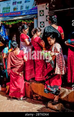 Kathmandu, Bhaktapur. Bunte Straßenszene mit den Damen in der hinduistischen Farbe Rot gekleidet, in der mittelalterlichen Stadt Bhaktapur aus dem 17. Jahrhundert mit Einheimischen, die Geschenke an Hindu-Schreine während des Bada Dasain Festivals platzieren Stockfoto