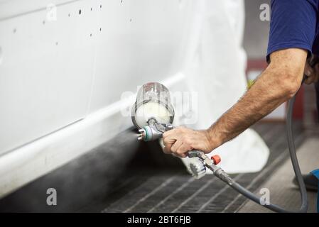 Nahaufnahme der männlichen Hand halten Spritzpistole und Malerei Fahrzeug in weißer Farbe. Gentleman demonstriert Farbsprühtechnik auf Automobil. Konzept der Auto-Service und Tuning. Stockfoto