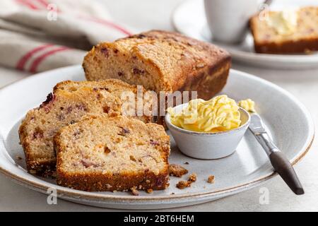 In Scheiben geschnittener Cranberry-Orangenkuchen und eine Schüssel Butter auf einem Teller Stockfoto