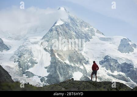 Horizontale Momentaufnahme des erstaunlichen, felsigen Ober Gabelhorn im Schnee in den Pennine Alpen in der Schweiz, zwischen Zermatt und Zinal, ein Tourist, der die Aussicht im Vordergrund genießt Stockfoto