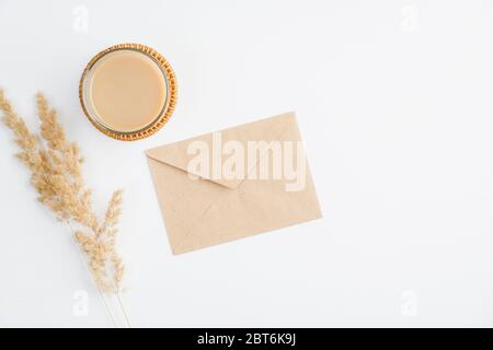 Flache Komposition mit handgefertem Papierumschlag, Tasse Kaffee und trockenen Blumen auf weißem Tisch. Herbst Herbst, romantisches Zeitkonzept. Stockfoto